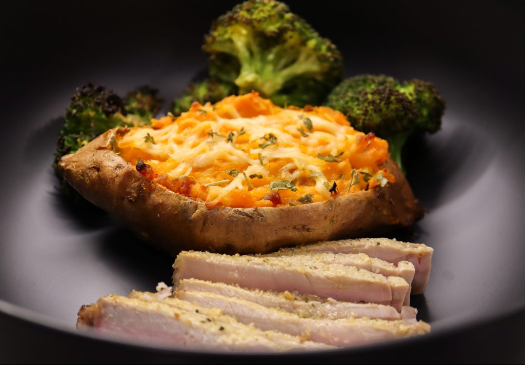 Twice Baked Sweet Potato with Broccoli and Sliced Pork Chops in Black Bowl